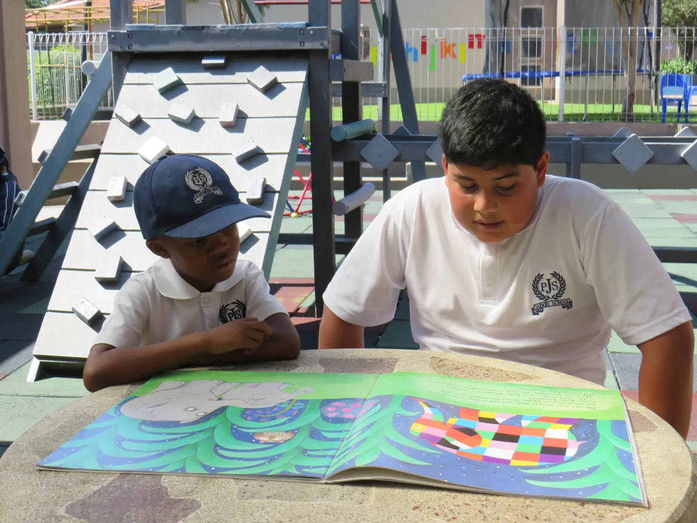 Two pupils reading a picture book together at an outdoor table
