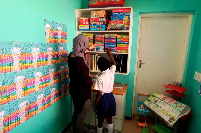 A teacher and a pupil choosing a learning game from the classroom shelf at Japari School